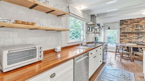 Une cuisine moderne avec des armoires blanches, des comptoirs en bois, un four encastré et un mur d’accent en briques.