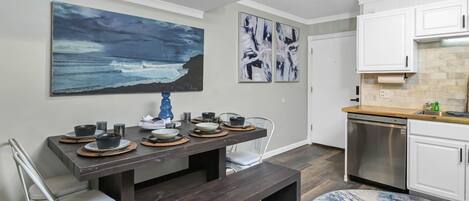 A modern kitchen with white cabinets, a stainless steel dishwasher, and a dining area with a dark wooden table set for four.