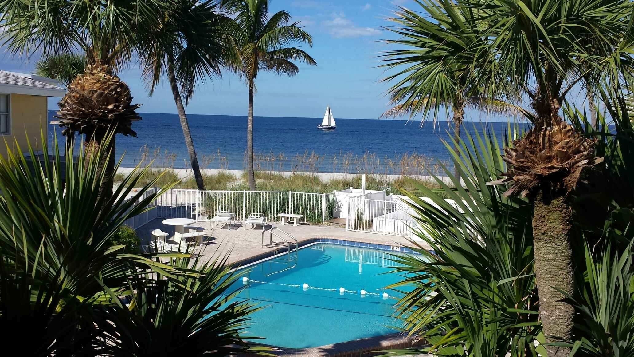 A pool area with a view of the ocean and a sailboat.