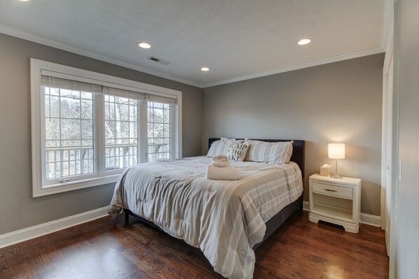 A bedroom with a large window, a bed with a pillow that says "Jump in the lake," and a nightstand with a lamp.