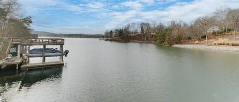 Un barco amarrado con zona de estar cubierta y un motor en un lago tranquilo, rodeado de árboles y un cielo despejado.