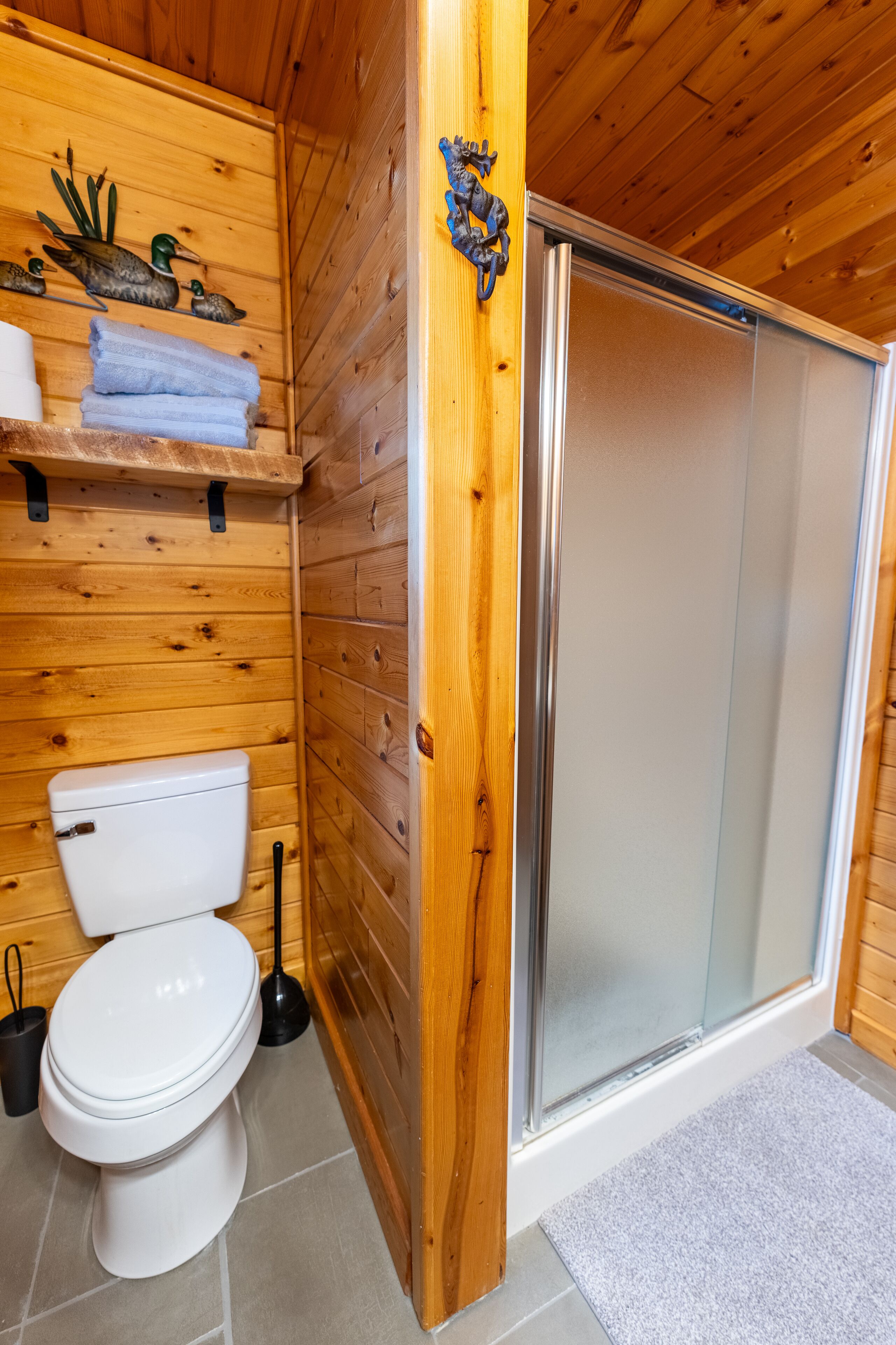 Une salle de bain en bois comprenant des toilettes, une douche et une étagère avec des serviettes.