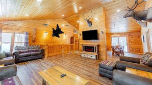 A log cabin interior with a fireplace, wooden walls, mounted animal heads, a sofa, and a television.