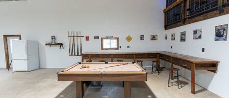 A pool table in a room with a wooden desk, a refrigerator, and a window.