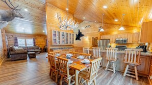 A wooden cabin interior with a dining area, kitchen, and living room.