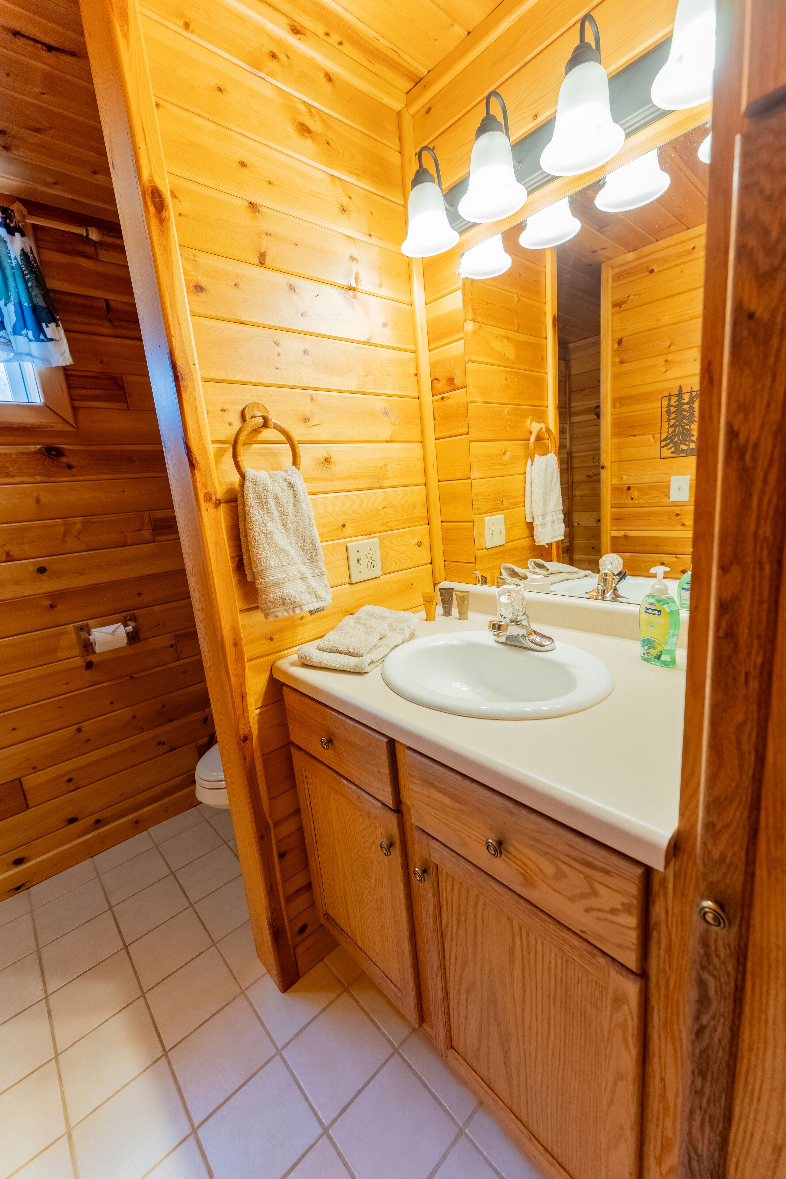 Ein Badezimmer einer Holzhütte mit Waschbecken, Spiegel und Pendelleuchten.