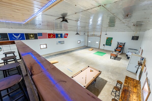 A spacious room with a pool table, bar area, and various flags on the walls.