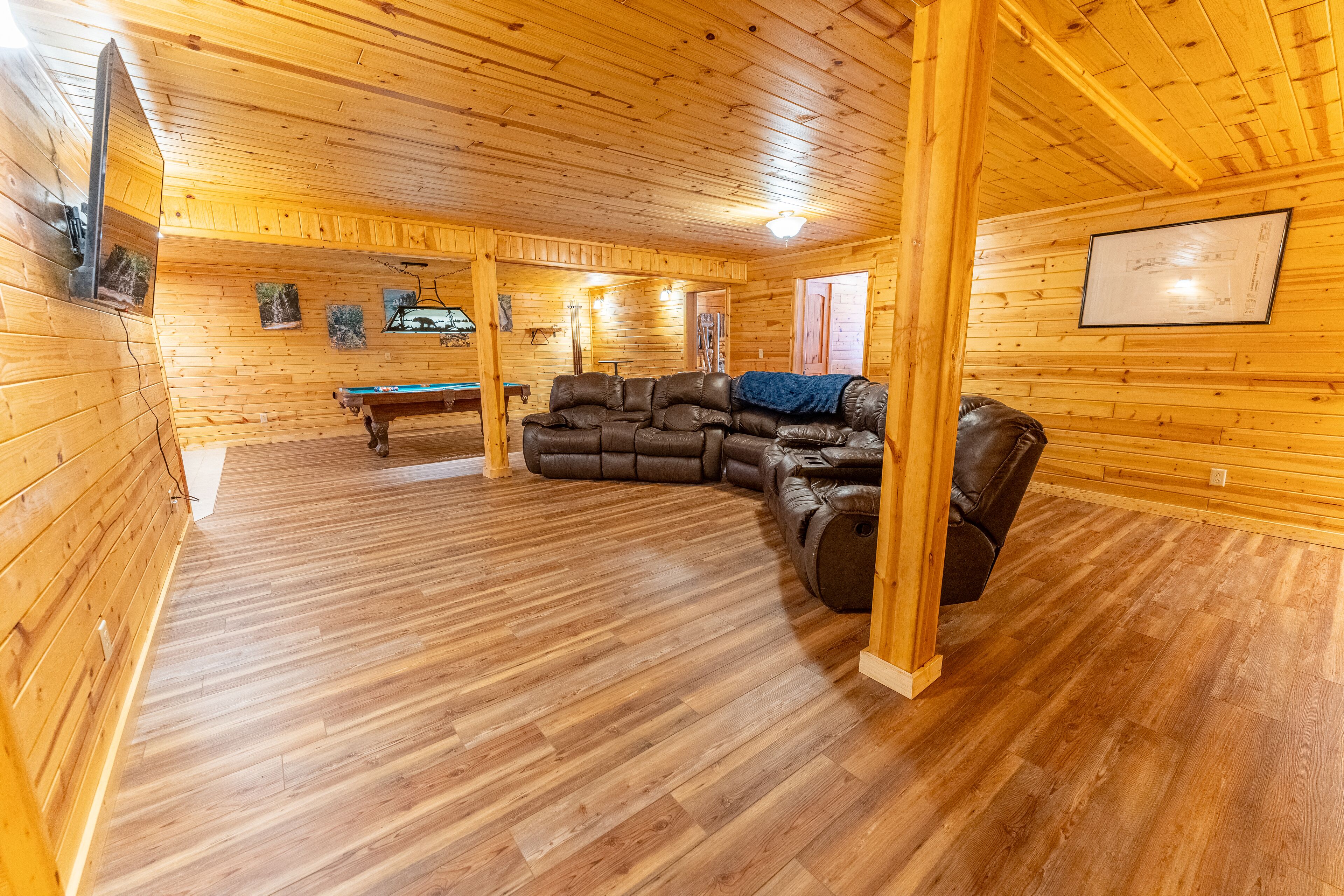 A wooden interior with a pool table, leather sofa, and a billiards table.