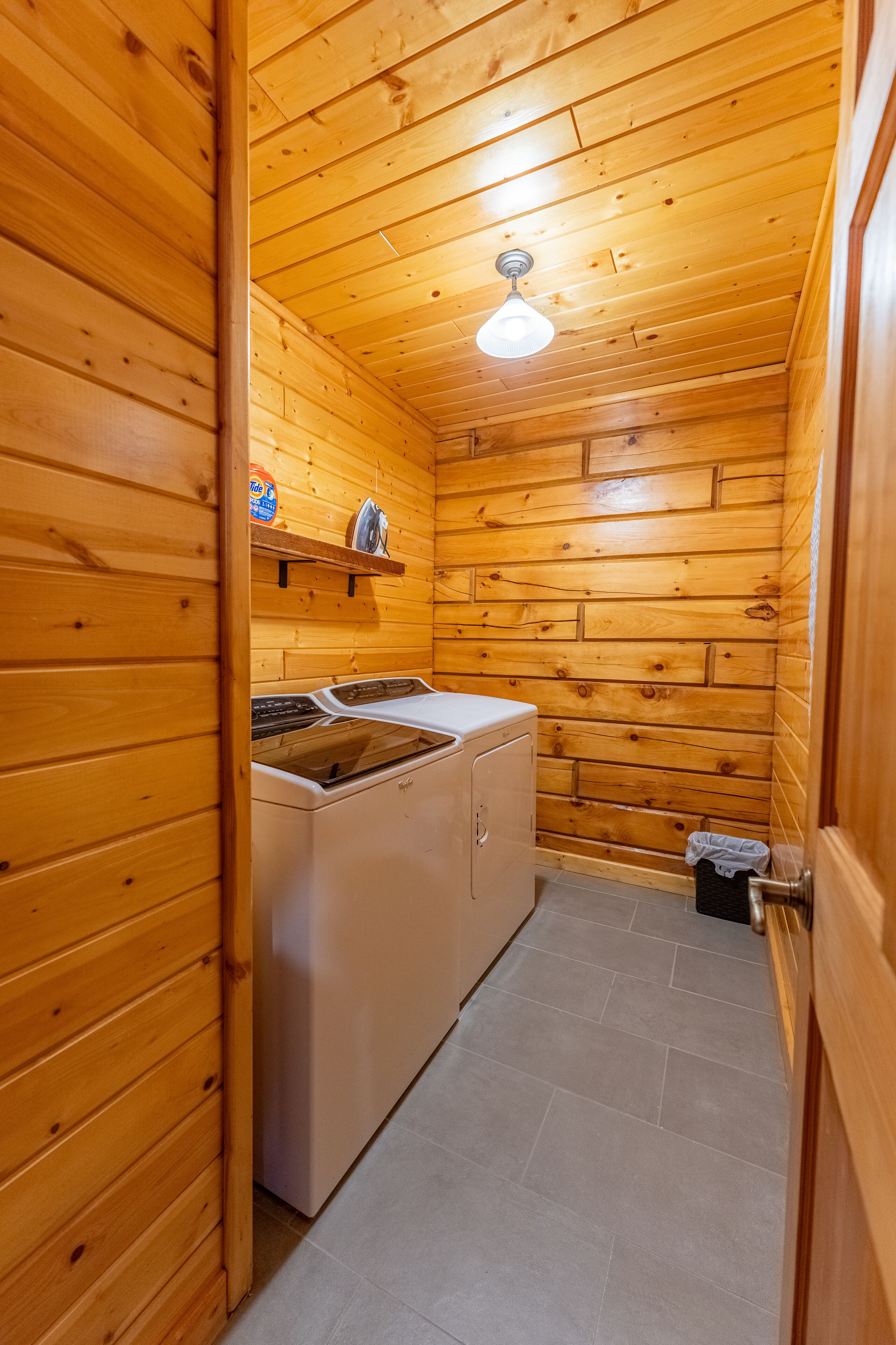 Cocina compacta con paredes de madera, lavadora y un pequeño estante con objetos.