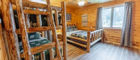 Een chalet met een vide, een ladder, een plafondventilator en een raam met gordijnen.