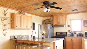 Una cocina con armarios de madera, encimera de granito, refrigerador, estufa y ventilador de techo.