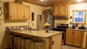 Una cocina con armarios de madera, encimera de granito, refrigerador de acero inoxidable, estufa y ventana con vista a árboles.