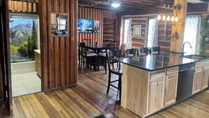 A rustic cabin interior with a wooden dining area, a kitchen with a large island, and a bathroom with a mountain view. - The little Log Lodge (City of the Village of Clarkston)