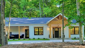 A two-story log cabin with a covered porch, large windows, and a well-maintained lawn. - Silver Lake & Dunes Dream House (Mears)