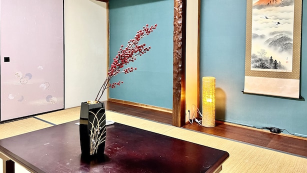 Een traditionele Japanse kamer met tatami vloerbedekking, een shoji scherm, een donker houten tafel, een vaas met rode bloemen, een lamp en een lijst met een berglandschap.