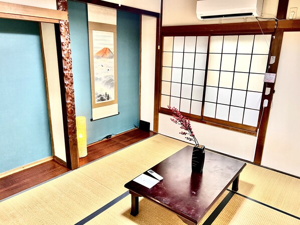 A traditional Japanese room with tatami flooring, a shoji screen, a sliding door, and a small table with a vase.