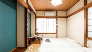 Een traditionele Japanse kamer met tatami vloerbedekking, een houten plafond en een schuifdeur van shoji-papier. Er staan twee bedden met witte beddengoed en een klein tafeltje met een vaas en een kom.