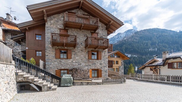 A stone building with wooden balconies and a cobblestone courtyard. - Casa Roberto (Moena)