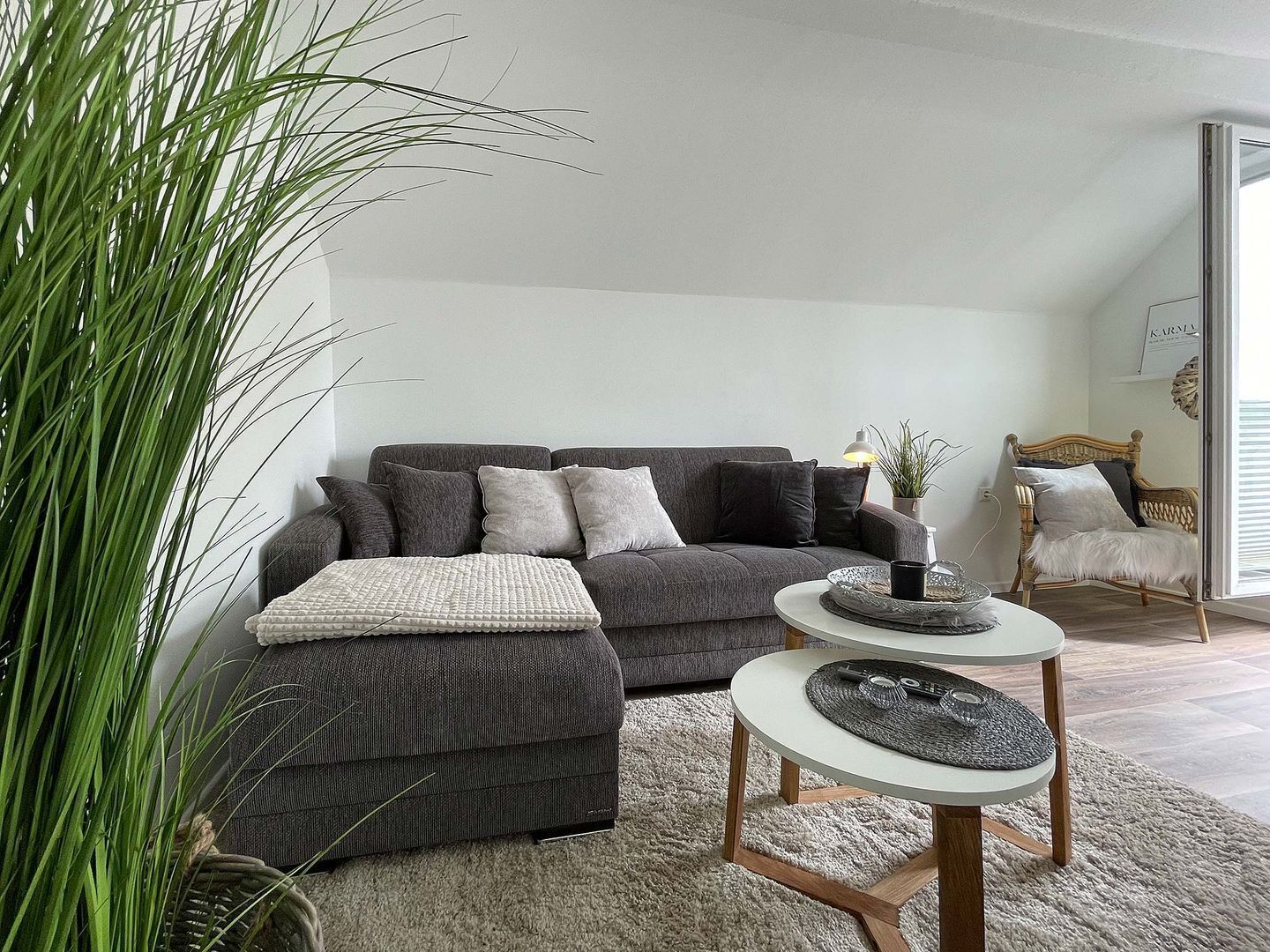 Een moderne woonkamer met een grijze bank, een ronde salontafel en een grote potplant.