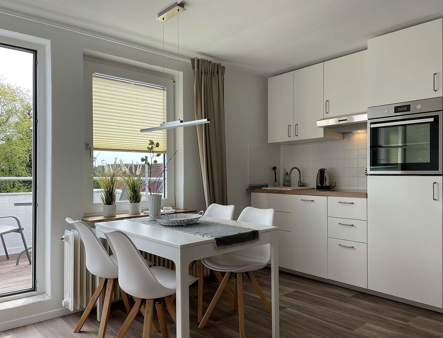 A modern kitchen with white cabinets, a built-in oven, and a dining area with a white table and chairs.