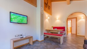 Una sala de estar con un televisor montado en la pared, un banco de madera, un sofá rojo y una mesa de comedor con sillas.