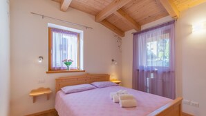 Un dormitorio con una cama de madera, una ventana con cortinas, una mesita de noche y una lámpara fijada a la pared.