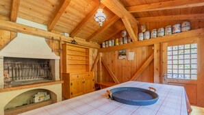 Una cabaña de madera con área de cocina, una mesa de comedor con mantel a cuadros y un estante con alimentos enlatados.