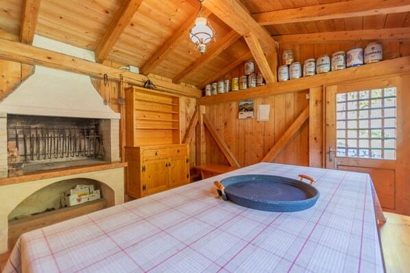 Une cabane en bois comprenant un coin cuisine, une table à manger recouverte d’une nappe à carreaux et une étagère remplie de conserves.