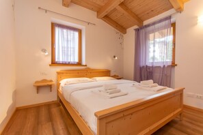 A bedroom with a wooden bed, two bedside tables, a window with curtains, and a wooden ceiling. - Villa Edelweiss Cardo (Alleghe)