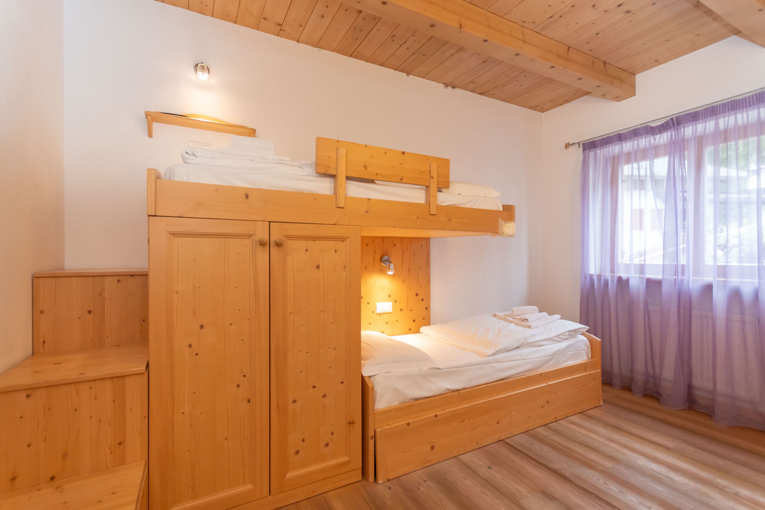 Une chambre avec un lit superposé, des murs et un plafond en bois, une fenêtre avec des rideaux et une lampe de chevet.