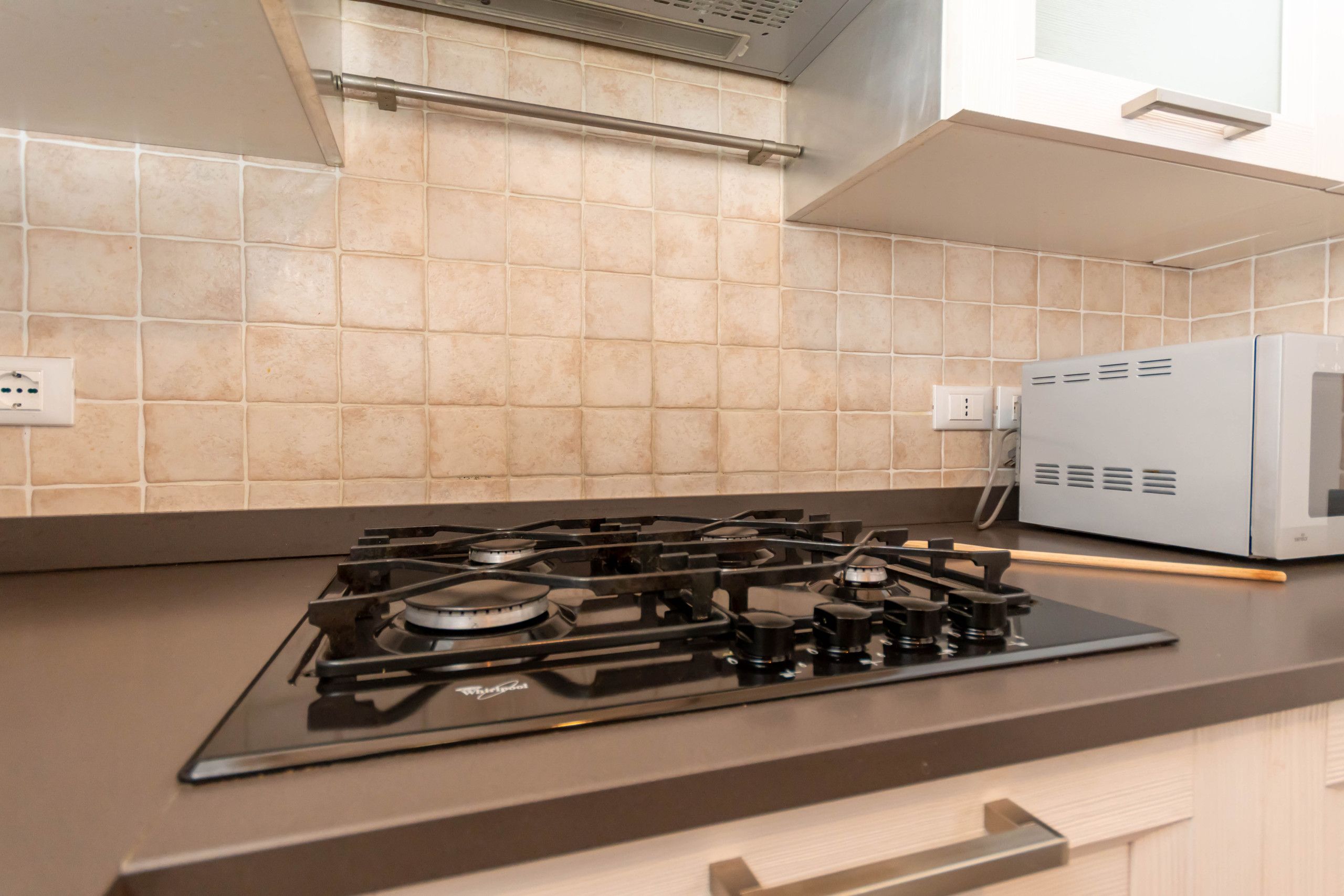 Una cocina con estufa a gas, microondas y paredes con azulejos color beige.