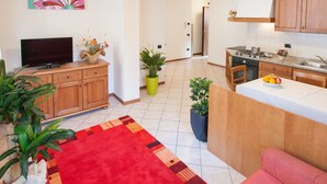 A modern kitchen with wooden cabinets, a built-in stove, and a dining area with a red rug and a small table. - Casa al Moro 2 (Rocca Pietore)