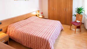 A bedroom with a bed, a nightstand, a wooden wardrobe, a chair, and a potted plant. - Casa al Moro 2 (Rocca Pietore)
