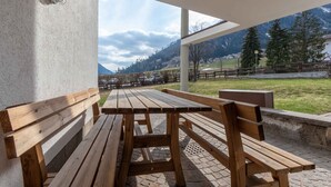An outdoor seating area with wooden benches and tables, overlooking a mountainous landscape.
