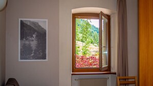 A room with a window, a radiator, a chair, and a table. - Regina 3 (Alleghe)