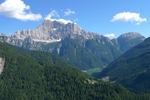 A mountainous landscape with a prominent rocky peak, dense forested valleys, and a small settlement in the valley. - Regina 3 (Alleghe)