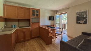 A compact kitchen with wooden cabinets, a built-in oven, and a dining area with a table and chairs. - Regina 9 (Alleghe)