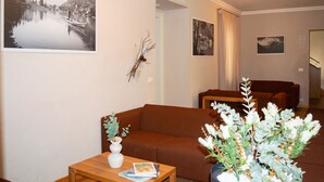 A living room with a brown sofa, a wooden coffee table with a vase and a book, and a wall with framed pictures. - Regina 9 (Alleghe)