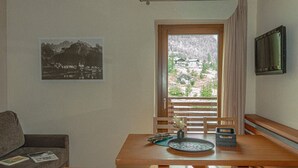 A room with a wooden table, a sofa, a TV, a window with curtains, and a framed picture on the wall. - Regina 12 (Alleghe)