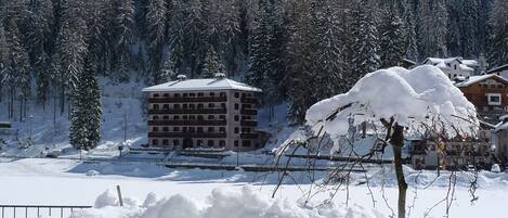 A snow-covered building with multiple balconies, surrounded by a snowy landscape and dense forest.