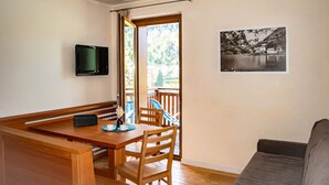 A room with a wooden dining table, chairs, a sofa, a TV, and a framed picture on the wall. - Regina 13 (Alleghe)