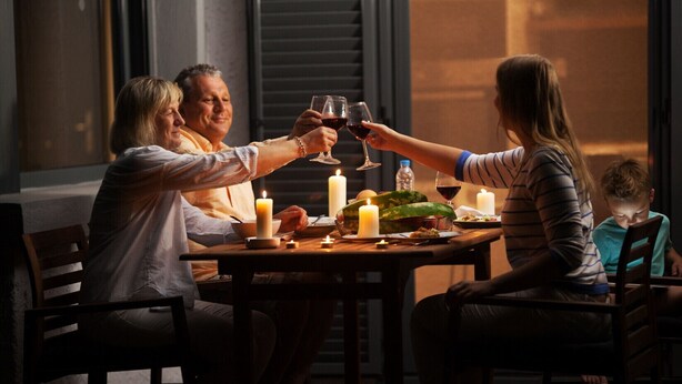 En familie spiser ved et bord med stearinlys, en flaske og et glas rødvin.