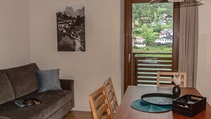 Una sala de estar con un sofá, una mesa de comedor con sillas, un cuadro en la pared y vistas a través de una puerta.