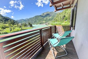 Un balcon donnant sur un lac et des montagnes, deux chaises vertes et une balustrade en bois.