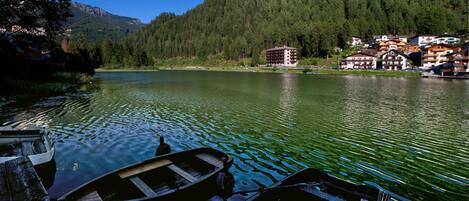 A lake with boats docked, surrounded by forested hills and a cluster of buildings with balconies.