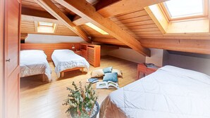 A loft bedroom with a sloped ceiling, wooden beams, and skylights. There are three beds, a small table, and a potted plant. - Regina 20 (Alleghe)