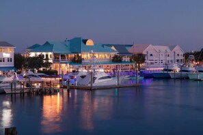 Un port de plaisance où sont amarrés plusieurs bateaux, un bâtiment avec un toit bleu et un bâtiment blanc doté d’un balcon.