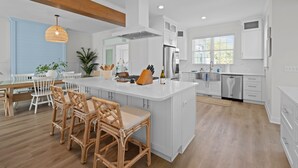 Een moderne keuken met witte kasten, een centraal eiland en een eethoek met rieten stoelen.