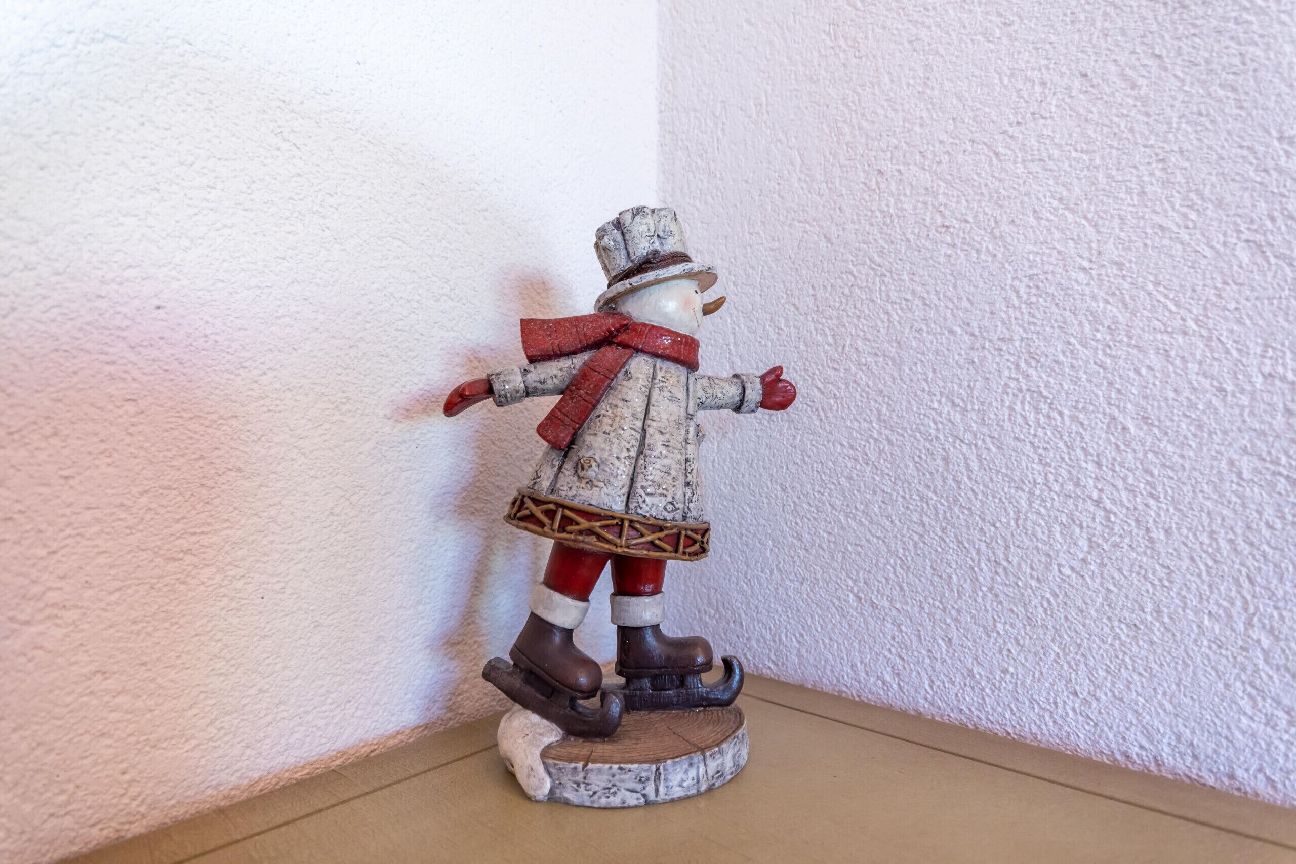 Una figurita de muñeco de nieve con sombrero, bufanda y botas sobre una base de madera.