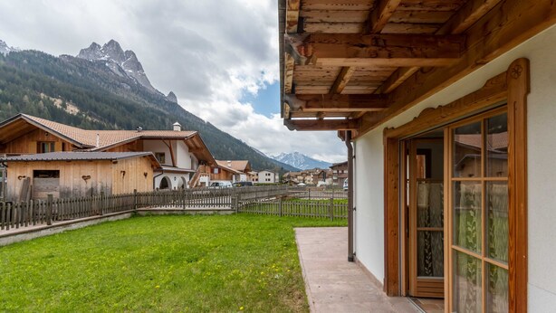 A traditional chalet with a wooden facade, a paved patio, and a mountain backdrop. - Casa De La Veisc (Pozza di Fassa)